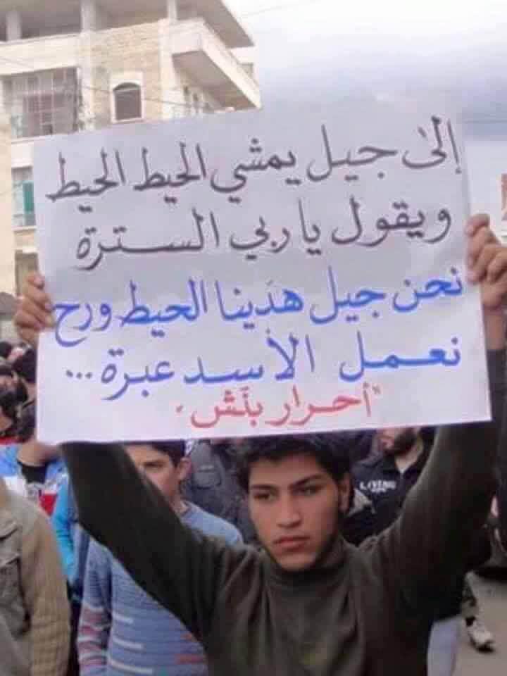 Young protestor holds placard reading: "To the generation who  lived in fear and spent their lives in caution. We are the generation that broke the walls of fear. We will make an example out of Assad"