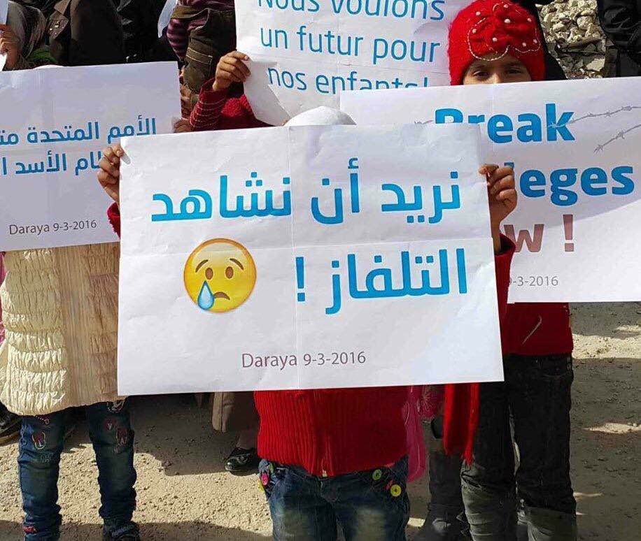  Child in Daraya holds sign saying "I want to watch TV!" 