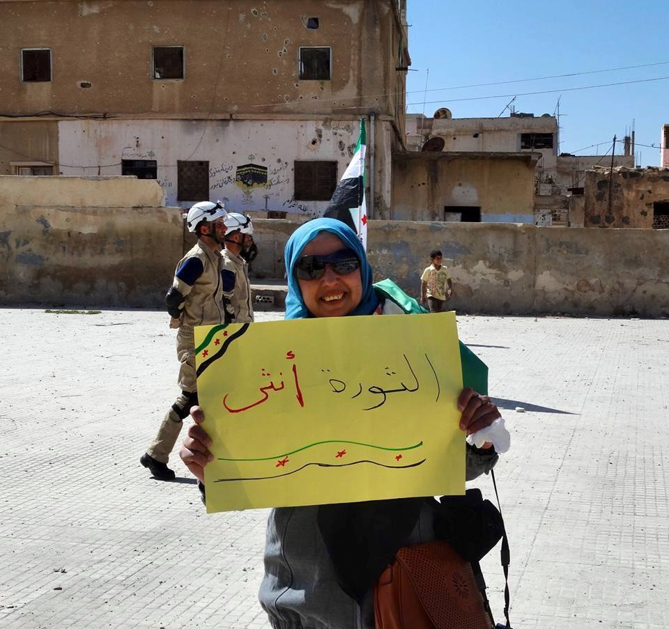 Woman in Daraa holds sign saying "The Revolution is Female" 